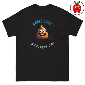 May include: A black short-sleeve t-shirt featuring a cartoon brown poop emoji character holding a small black briefcase. The text above the character reads SAME SHIT, and the text below the character reads DIFFERENT DAY! in a light green color.