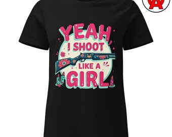 Puede incluir: Camiseta negra con el texto "YEAH I SHOOT LIKE A GIRL" en rosa y turquesa. El diseño incluye una escopeta decorada con flores y velas. Una camiseta gráfica audaz.