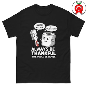 May include: Black t-shirt with a humorous graphic featuring a toothbrush and a roll of toilet paper with speech bubbles. The text reads "I hate my job," "Oh please!!!!," "Always be thankful," and "Life could be worse."
