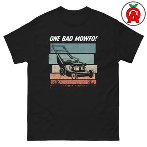 May include: Black t-shirt with a graphic of a lawn mower and the text "ONE BAD MOWFO!". The design features a lawn mower illustration with a retro color scheme of blue, teal, and orange stripes, and grass at the bottom.
