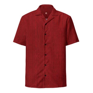 May include: A short-sleeved red shirt with a vertical stripe pattern. The shirt has a camp collar, a button-down front with black buttons, and a small logo near the top button. The fabric appears to have a subtle texture.