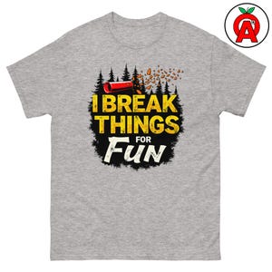Könnte beinhalten: Ein graues T-Shirt mit einem Grafikdesign eines roten und schwarzen Feuerwerks, das in einem Wald explodiert. Der Text "I Break Things For Fun" ist in gelben und schwarzen Buchstaben geschrieben.