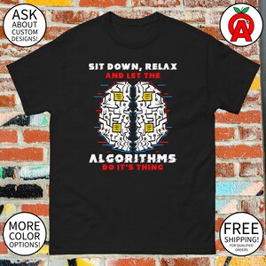 May include: Black t-shirt with a graphic of a brain composed of circuit board elements. The text reads "SIT DOWN, RELAX AND LET THE ALGORITHMS DO IT'S THING." Additional text on the shirt says "ASK ABOUT CUSTOM DESIGNS!" and "MORE COLOR OPTIONS!"