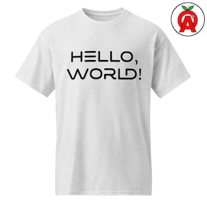 May include: A light gray short-sleeved t-shirt featuring the black text "HELLO, WORLD!" printed across the chest in a modern, rounded sans-serif font. The shirt has a crew neckline and a standard fit, with a small circular logo in the top right corner.