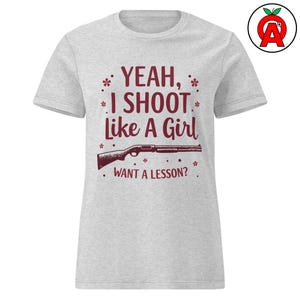 Puede incluir: Camiseta gris claro con el texto burdeos "YEAH, I SHOOT Like A Girl WANT A LESSON?" y un gráfico de escopeta burdeos. La camiseta tiene cuello redondo y mangas cortas.