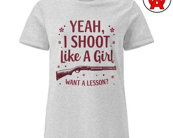Puede incluir: Camiseta gris claro con el texto burdeos "YEAH, I SHOOT Like A Girl WANT A LESSON?" y un gráfico de escopeta burdeos. La camiseta tiene cuello redondo y mangas cortas.
