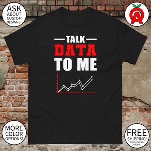 Puede incluir: Camiseta negra con el texto "TALK DATA TO ME" en blanco y rojo, junto con un gráfico de líneas. La camiseta también tiene texto y logotipos adicionales en las esquinas.