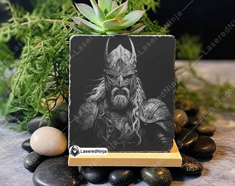 May include: Black and white engraved image of a Viking warrior wearing a horned helmet and armour. The image is on a black slate coaster with a wooden base.