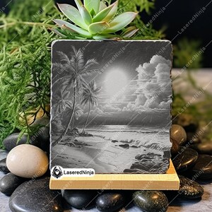 May include: A black slate coaster with a laser-engraved image of palm trees on a beach with a sunset and clouds. The coaster is on a wooden stand.