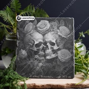 May include: A black slate coaster with a laser-etched design of two skulls intertwined with roses. The design is in shades of gray and white.