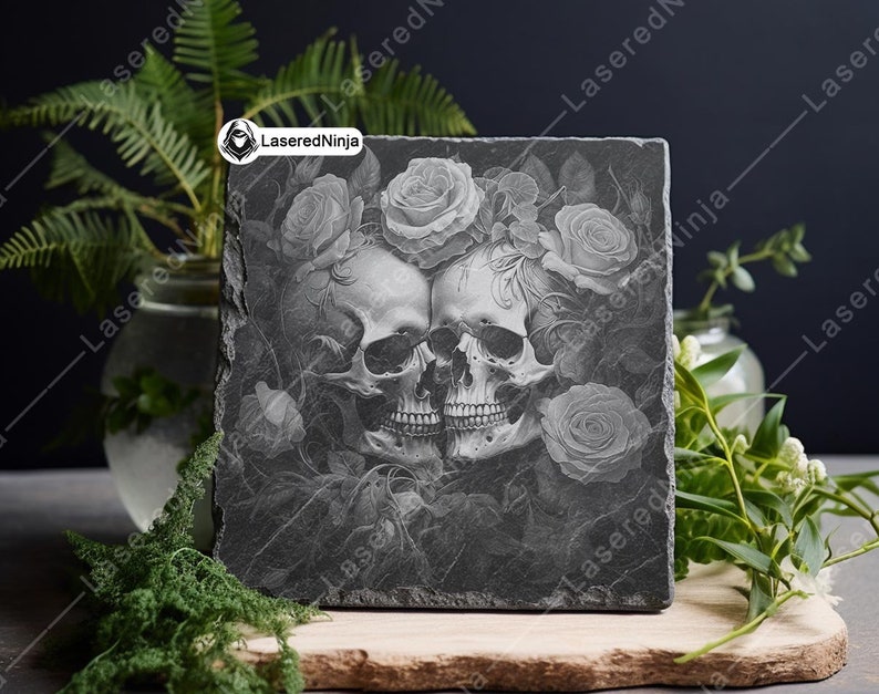 May include: A black slate coaster with a laser-etched design of two skulls intertwined with roses. The design is in shades of gray and white.