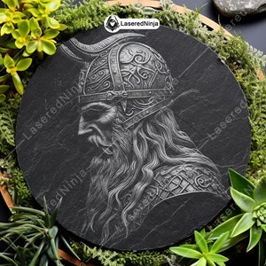 May include: A black and white engraved image of a Viking warrior with a horned helmet and a long beard. The image is on a round black slate plaque.
