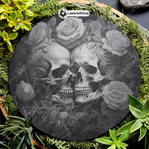 May include: Black and white engraved image of two skulls intertwined with roses on a round black slate coaster. The image is in a gothic style.