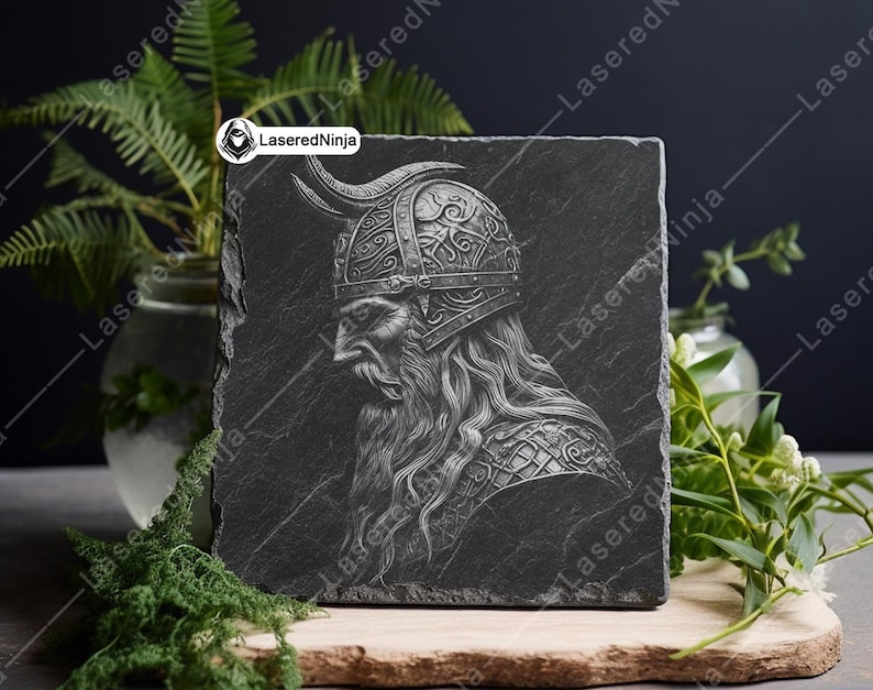 May include: A black slate coaster with a detailed engraving of a Viking warrior wearing a horned helmet. The engraving is in a silver color.