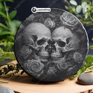 May include: A black slate coaster with a laser-etched design of two skulls with intricate details, surrounded by roses. The coaster is round and has a smooth, polished surface.
