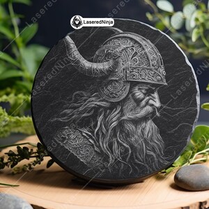 May include: A black slate coaster with a detailed engraving of a bearded warrior wearing a horned helmet. The engraving is in a white color and the warrior is looking to the right.