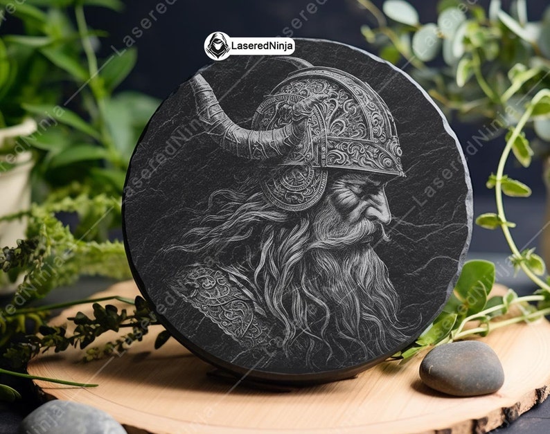 May include: A black slate coaster with a detailed engraving of a bearded warrior wearing a horned helmet. The engraving is in a white color and the warrior is looking to the right.