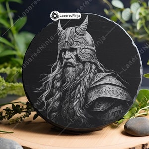May include: A black and white engraved image of a warrior with a long beard and a horned helmet. The image is on a round black slate coaster.