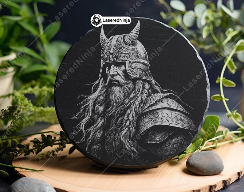 May include: A black and white engraved image of a warrior with a long beard and a horned helmet. The image is on a round black slate coaster.