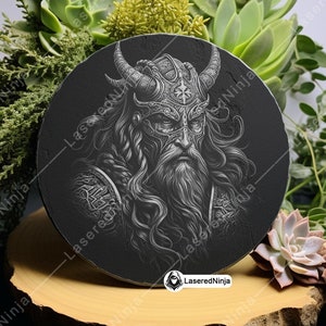 May include: A black and white circular coaster featuring a detailed image of a Viking warrior wearing a horned helmet. The warrior has a long beard and is looking straight ahead. The coaster is made of slate and has a smooth, polished surface.