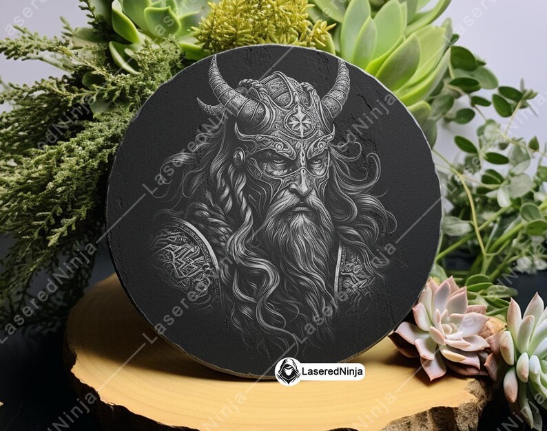 May include: A black and white circular coaster featuring a detailed image of a Viking warrior wearing a horned helmet. The warrior has a long beard and is looking straight ahead. The coaster is made of slate and has a smooth, polished surface.