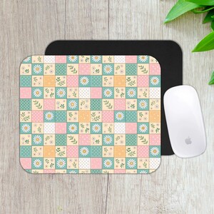Peut inclure: Un tapis de souris floral avec un motif patchwork. Le tapis de souris présente un motif de carrés aux couleurs pastel, dont le rose, le bleu et le jaune, chacun orné de marguerites et de feuilles. Un tapis de souris noir et une souris blanche sont également visibles.
