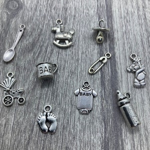 May include: A set of ten silver charm pendants with baby-themed designs, including a rocking horse, a baby bottle, a dummy, a baby onesie, a baby carriage, a spoon, a cup, a pair of footprints, a safety pin, and a teddy bear holding a flower.