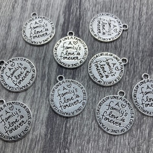 May include: A selection of silver-coloured, round charms. Each charm is inscribed with the words "A family's love is forever" in a circular pattern. The charms have a small loop at the top for attaching to jewellery or other crafts.