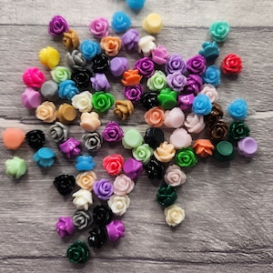 May include: A large collection of colourful plastic rose-shaped embellishments. The roses are in various shades of pink, purple, blue, green, yellow, orange, and red.
