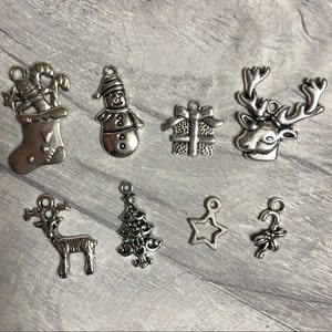 Pode incluir: Um conjunto de dez pingentes de prata com vários temas natalinos, incluindo um boneco de neve, uma meia, uma rena, uma estrela, uma árvore de Natal e um bastão de caramelo.