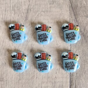 May include: Six blue and white mug-shaped resin charms with a pencil, ruler, and paintbrush design. Each charm says "Best Teacher Ever" in black text.