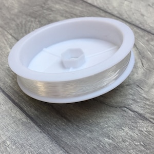 May include: A spool of clear elastic thread wound around a white plastic bobbin.