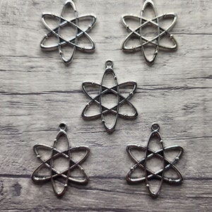 May include: Five silver atom charm pendants. Each charm is a stylised representation of an atom with a central circle and orbiting electrons.