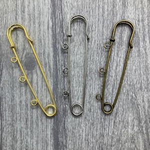 May include: Three safety pins with different finishes: gold, silver, and bronze. Each pin has four loops for attaching to fabric.