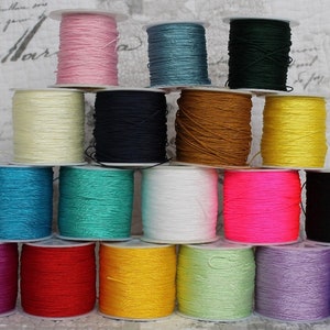 May include: A collection of 18 spools of colourful waxed cotton cord, arranged in a pyramid shape. The cords are in various colours, including pink, blue, green, yellow, red, purple, and black.