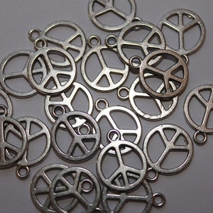 May include: A pile of silver peace sign charms. The charms are all the same size and shape, and they have a hole at the top for attaching to a necklace or bracelet.