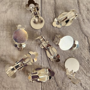 May include: Eight silver-toned earring clip-on backs with a flower design. The backs are designed to hold a round cabochon.