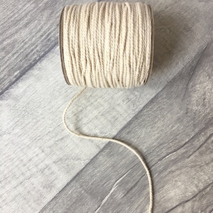 May include: A spool of natural cotton twine, wound tightly and ready to be used for crafting, wrapping, or macrame projects.
