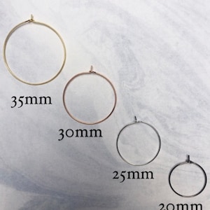 May include: Four hoop earrings in gold, rose gold, silver, and black. Sizes are 35mm, 30mm, 25mm, and 20mm. The earrings are displayed on a light grey and white marbled background.