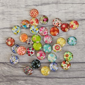 May include: Assortment of colourful round glass cabochons with floral patterns. Each cabochon features a different design with a variety of colours, including red, blue, green, yellow, and pink.