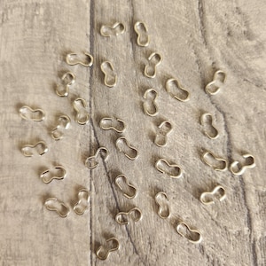 May include: A close-up of a group of silver-toned metal S-shaped hooks on a light brown wooden surface.