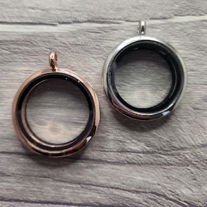May include: Two round silver locket pendants with glass inserts. One pendant is silver and the other is rose gold.