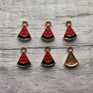 May include: Six gold-tone charms featuring watermelon slices. Three charms have red watermelon slices with black seeds and a green rind. Three charms have a gold-tone finish.