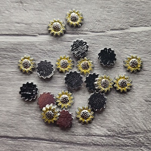 Peut inclure: Un ensemble de petits charmes argentés représentant des tournesols aux pétales jaunes et aux centres noirs. Certains charmes sont noirs unis.
