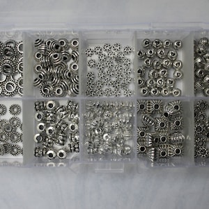 May include: A clear plastic storage box filled with ten compartments containing silver metal beads of various shapes and sizes.