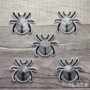 Puede incluir: Cinco parches de hierro bordados en plata y negro de un insecto garrapata.