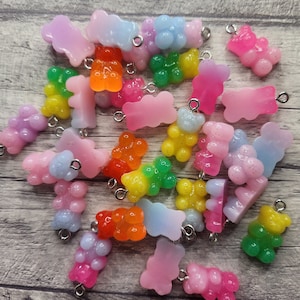 Puede incluir: Una colección de abalorios de ositos de goma de colores con anillas de salto plateadas. Los abalorios son de varios tonos de rosa, azul, verde, amarillo y naranja. Algunos de los abalorios tienen purpurina incrustada en la resina.