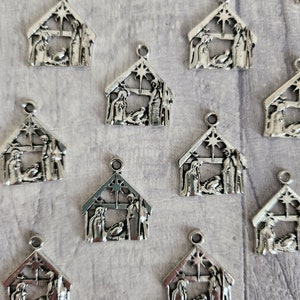May include: Silver metal nativity scene charms. Each charm shows the holy family inside a house-shaped frame, with a star at the top. These charms are suitable for crafting Christmas-themed jewellery or decorations.