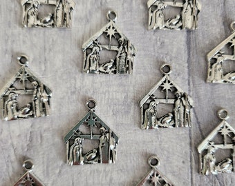 May include: Silver metal nativity scene charms. Each charm shows the holy family inside a house-shaped frame, with a star at the top. These charms are suitable for crafting Christmas-themed jewellery or decorations.