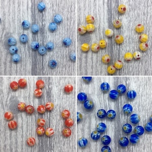 May include: Assortment of colourful glass beads with floral patterns. The beads are in shades of blue, yellow, and red.